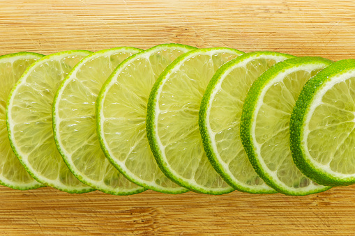 Closeup photo of fresh green lime slices over a wooden surface.