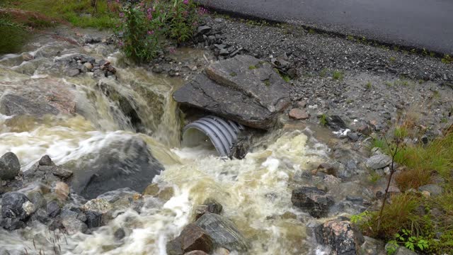 Rainwater rushes into culvert running under road during flooding in Norway.