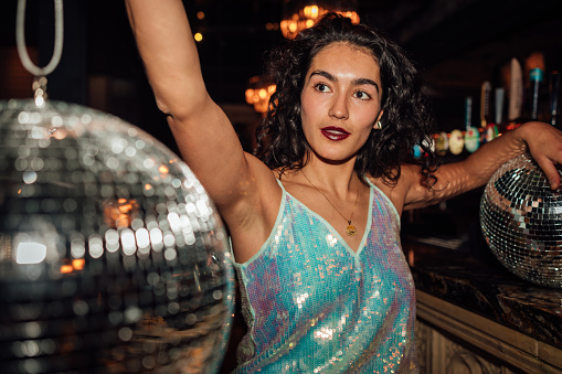 A medium close up portrait of a young woman who is wearing a shiny glitter dress and is holding up two glitter balls and is out with her friends celebrating New Years Eve in the North East of England.