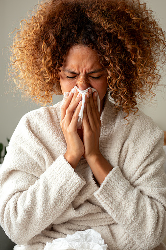 young woman feeling ill and blowing her nose with a tissue