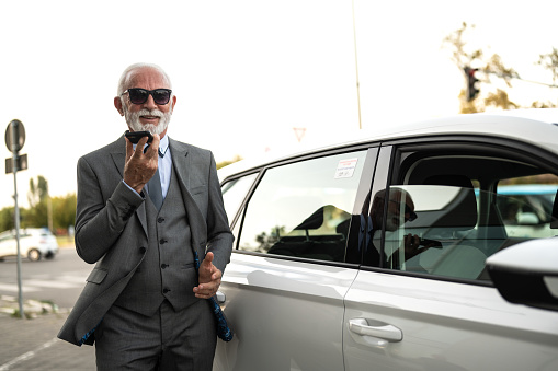 Senior business man standing next to his car, having a phone call