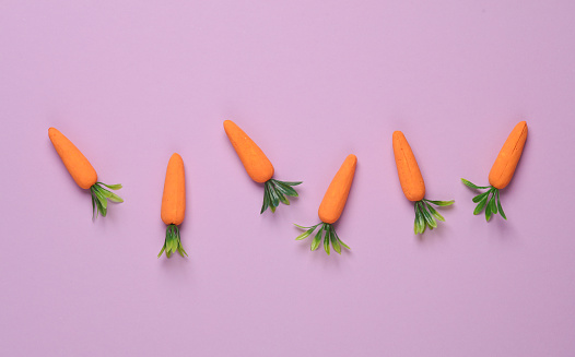 Plastic miniature carrot on a pastel background. Minimal, conceptual food still life