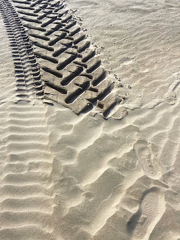 Perspective of tyre tracks on sandy beach with dark blue cloudy sky
