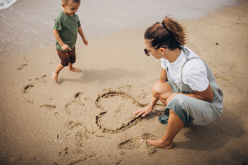 Woman playing with her little son on the beach by the sea, they are on vacation.