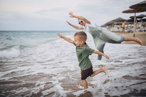 Woman playing with her little son on the beach by the sea, they are on vacation.