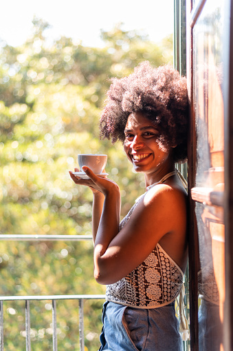 Vertical photo of a mixed race smiling woman with a cup of coffee at home