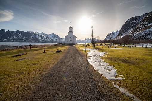 The small wooden white church in Gimsøy on the beach on the Lofoten islands in Norway in winter with beautiful old cemetery and mountains Vagan Nordland Norway