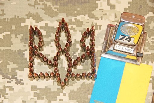 coat of arms of Ukraine laid out from cartridges on background of camouflage clothing and dark sky. Cartridges for the Kalashnikov assault rifle. War Concept. Ukrainian national symbol