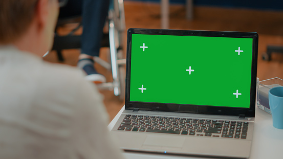 Senior woman using modern laptop with green screen. Retired adult analyzing isolated chroma key and blank copy space template with mock up background on computer display. Technology
