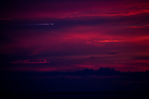 Airplane silhouette flying above a dramatic purple sunset, Portugal.