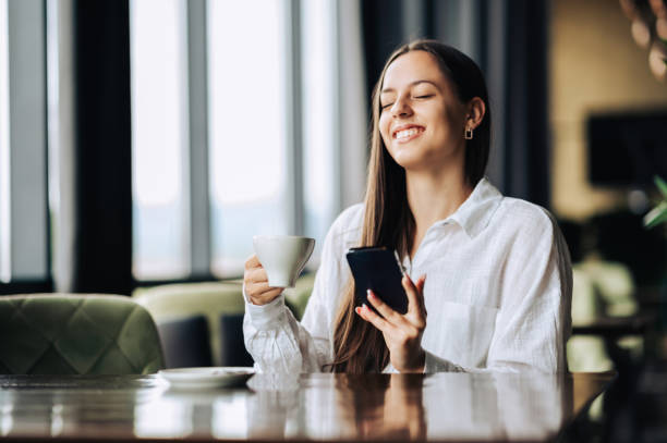 istock A young woman is sitting in a cafe and enjoying coffee while using her phone. 1702724635