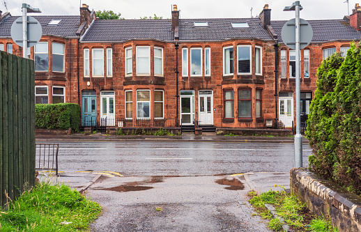 A view from a lane towards red sandstone terraced houses on Crow Road in Glasgow, Scotland.