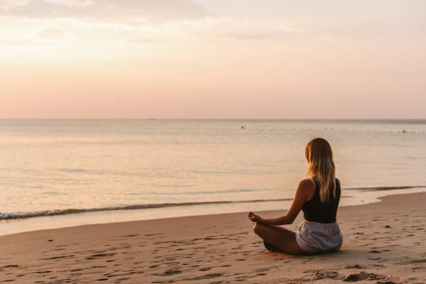 istock Woman meditating on the beach at sunset 1702735241