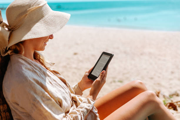 istock Woman with an e-reader on vacation at the beach reading a book 1702735467