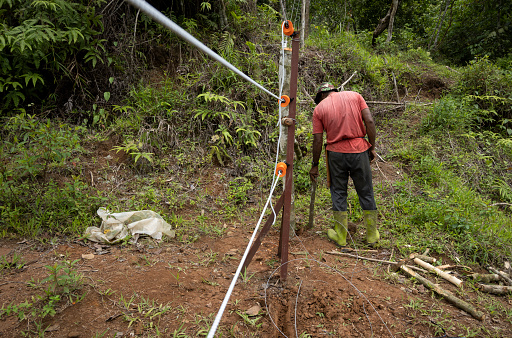 Man strikes a wooden stake to support a shock fence installed to deter wildlife from entering the farm.