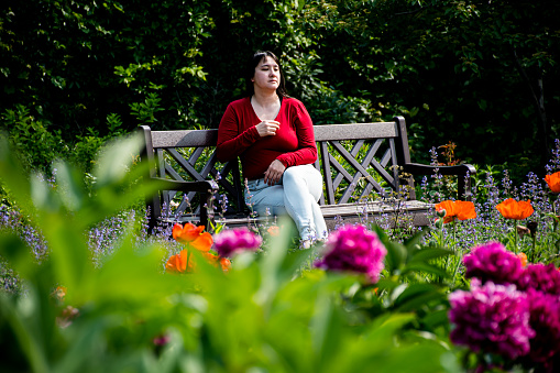 Surrounded by a kaleidoscope of colors, a 40-year-old  woman experiences a moment of serenity on a garden bench, captivated by the enchanting allure of blooming flowers.