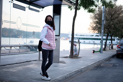 Young woman with a protective mask at a bus stop waiting her transport