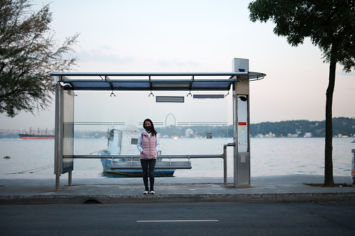 Young woman with a protective mask at a bus stop waiting her transport