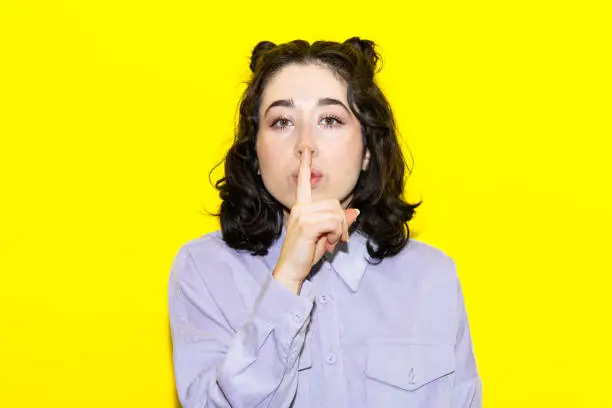 Photo of Young latin woman standing over yellow background asking to be quiet with finger on lips. silence and secret concept.