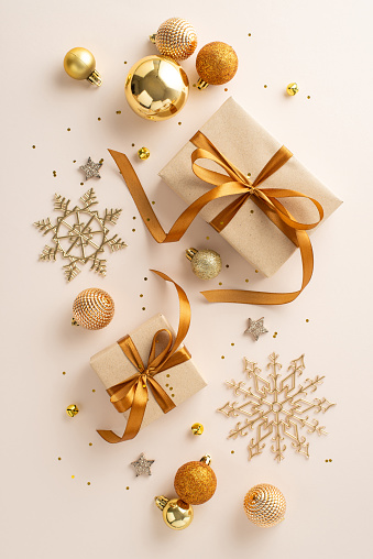 Christmas gift inspiration featuring artisanal gift boxes, ribbon bows, chic orange and gold baubles, shiny stars, snowflake decor, and confetti on a gentle pastel surface. Vertical top view image