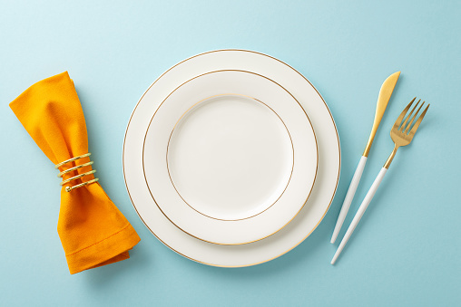 Above view captures the essence of a family Thanksgiving dinner setting during the fall season. Gilded tableware, classic cutlery on a blue isolated background, inviting text or promotional content