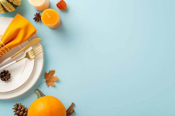 istock Fall-inspired Thanksgiving feast is portrayed from an aerial standpoint. Gilded table settings, vintage cutlery and decor on light blue isolated backdrop, ample space for text or adverts 1702909693