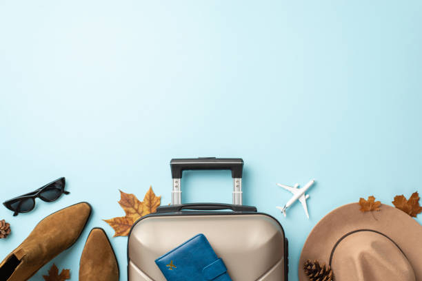 istock Your autumn journey, your elegance. Top-down view featuring a gray suitcase with passport, trendy boots, chic sunglasses and felt hat on light blue isolated backdrop, ready for your travel message 1702909740