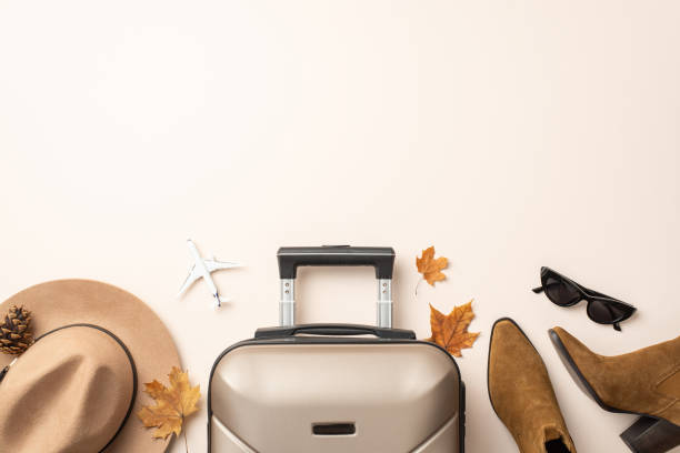 istock Airborne autumn femininity. Top view miniature plane, fashion-forward elements: felt hat, cat-eye shades, western boots, travel case, maple leaves, pine cone on soft neutral surface with ad space 1702909742