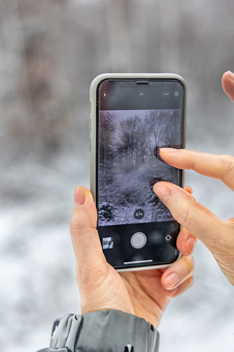 Woman shooting winter landscape with smartphone, display and hands close-up