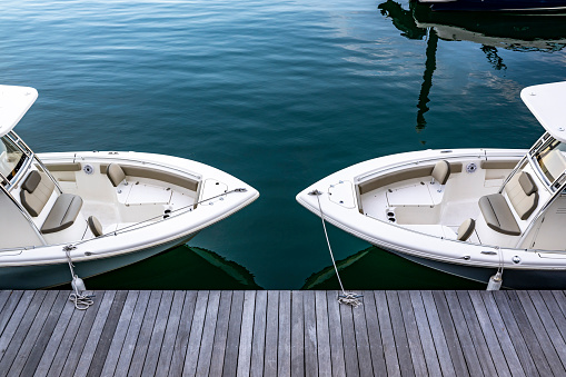 Two white identical boats with covered cabin moored in Boston Harbor with wooden piers protruding into the Atlantic Ocean with port trade and fishing infrastructure at twilight