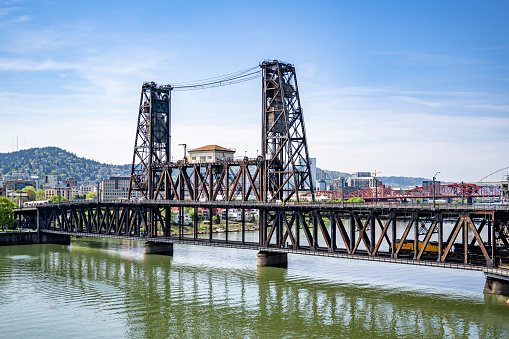Drawbridge transport and pedestrian Hawthorn bridge over the Willamette River in Portland with interlocking metal trusses and concrete supports and a view of the city down town with a cloudy sky