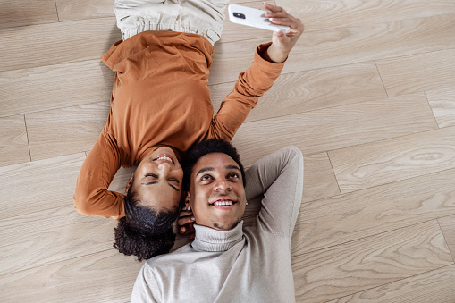 High-angle view of a young couple relaxing on the floor and taking a selfie with a mobile phone after moving into a new cozy apartment