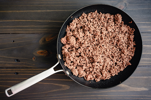 Cooked ground beef in a large non-stick frying pan on a wooden table