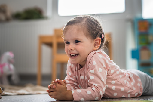 One toddler girl laying on the floor at home and smiling, learning and play, early child development concept