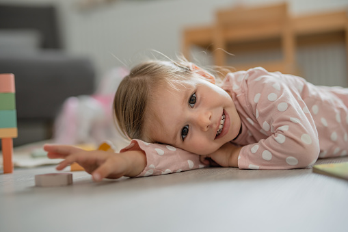 One toddler girl laying on the floor at home and smiling, learning and play, early child development concept