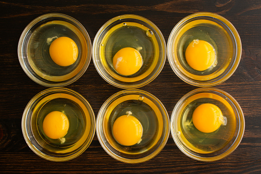 Six cracked eggs in small glass bowls on a wooden table
