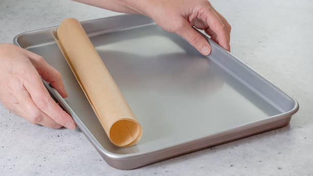 istock Woman's hands placing parchment paper onto a baking pan, close-up 1702989625