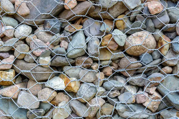 A closeup of a wire and rock retaining wall. The wire forms hex shaped holes with a variety of rock behind.