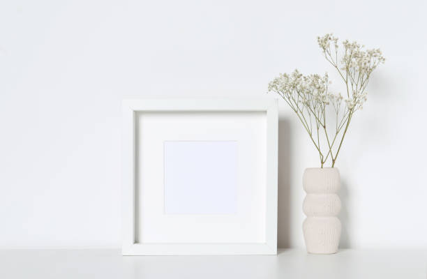 istock Empty photo frame and vase with dry decorative gypsophila flowers on white table. Mockup for design 1703045771