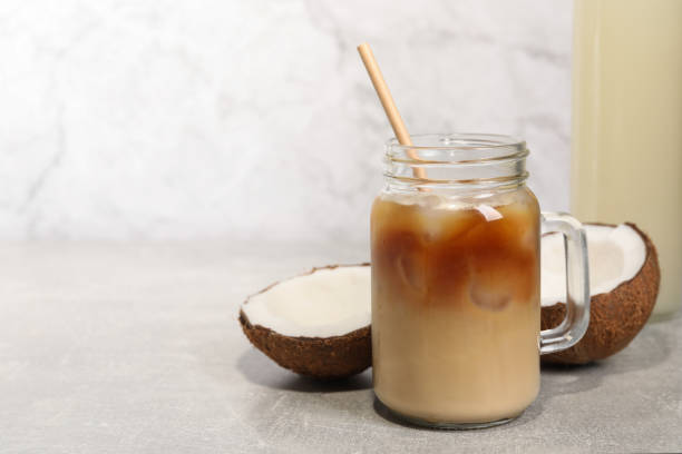 istock Mason jar of delicious iced coffee with coconut syrup on light grey table. Space for text 1703046221