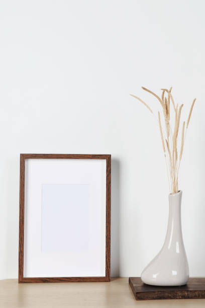 istock Empty photo frame and vase with dry decorative spikes on wooden table. Mockup for design 1703046345