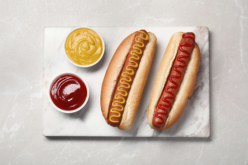Fresh delicious hot dogs with sauces on light grey marble table, top view