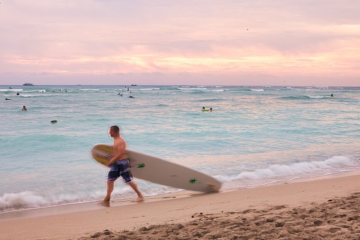 Honolulu, United States, December 06 2012 : a surfer is walking on the beach near the surf with surfboard passig a lifeguard post on Waikiki