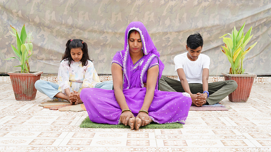 Mom teaches child to meditate. Young woman with her kids  doing yoga exercise outdoor at the day time.