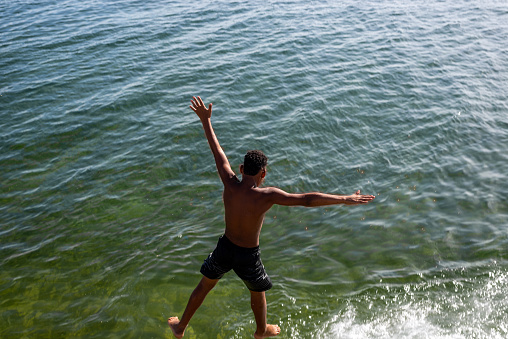 Salvador, Bahia, Brazil - December 31, 2021: A young man is seen jumping into the waters of Praia da Boa Viagem in the city of Salvador, Bahia.
