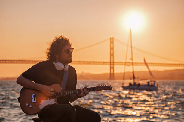 Street musician playing electric guitar in the street Hipster street musician in black playing electric guitar in the street on sunset with bridge and yacht boat in background yacht rock music stock pictures, royalty-free photos & images