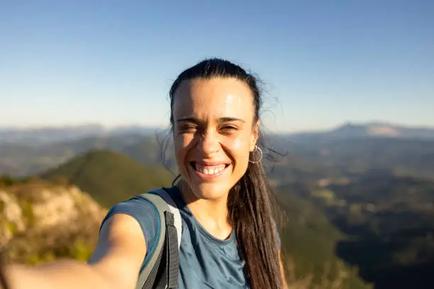 Photo of A young woman smiles at the sun from the top of a mountain near Pgasarri in the Basque Country