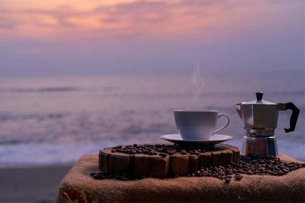 istock Close-up white coffee cup and many coffee beans placed around on wood table with a beautiful seascape 1703186473