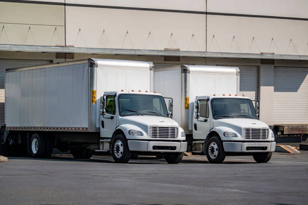 istock Day cab middle duty rig semi trucks with long box trailers loading cargo standing side by side in warehouse dock gates 1703196138