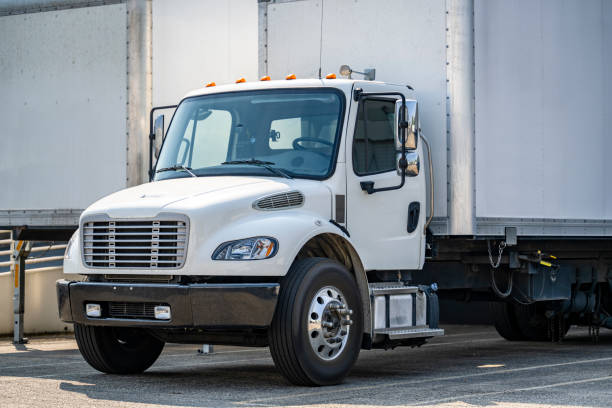 istock White compact middle duty day cab rig semi truck with box trailer loading cargo for the next delivery standing in warehouse dock with gates and another trailers 1703202844